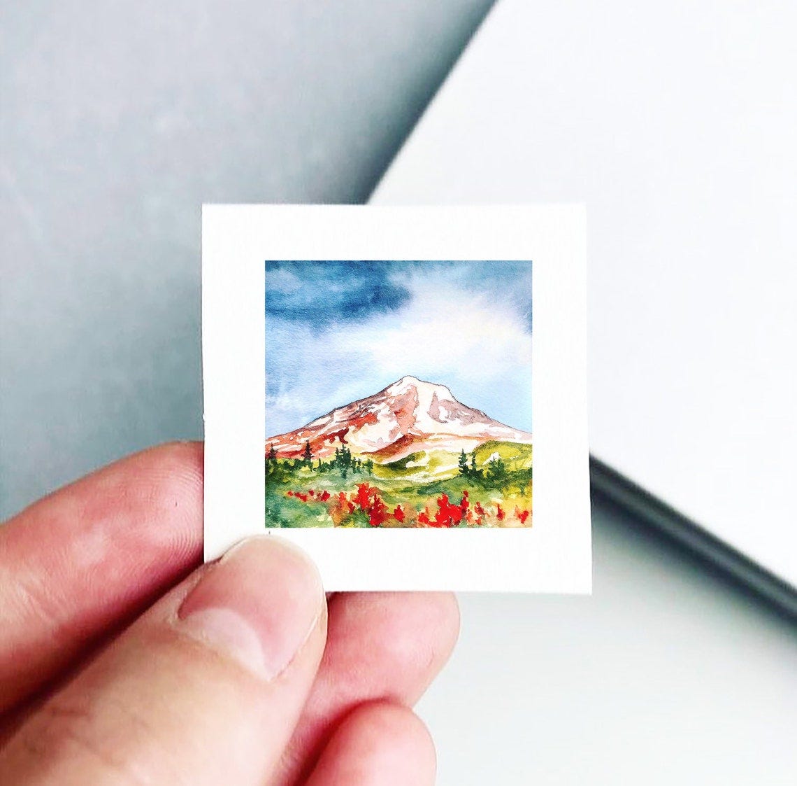 May include: A watercolor painting of a mountain with snow on the peak. The mountain is surrounded by green trees and red flowers. The sky is blue with white clouds. May include: A watercolor painting of a mountain with snow on the peak. The mountain is surrounded by green trees and red flowers. The sky is blue with white clouds.