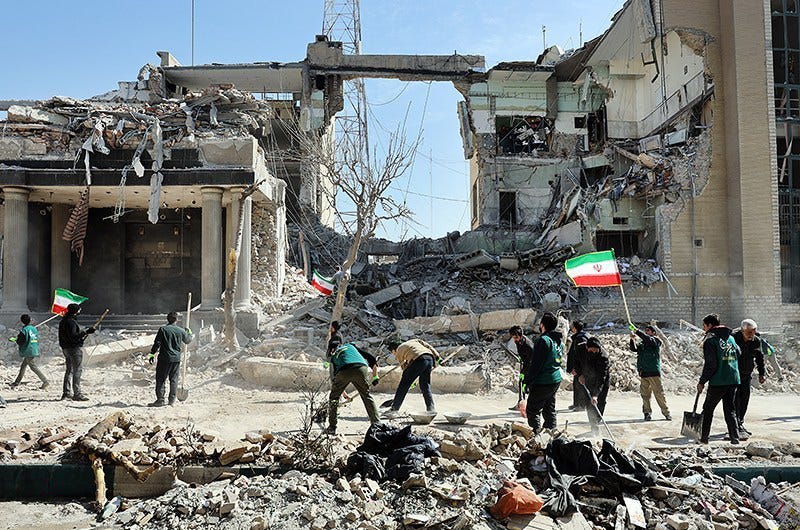 Destroyed buildings, men cleaning up with shovels and tools; one man waves an Iranian flag Destroyed buildings, men cleaning up with shovels and tools; one man waves an Iranian flag