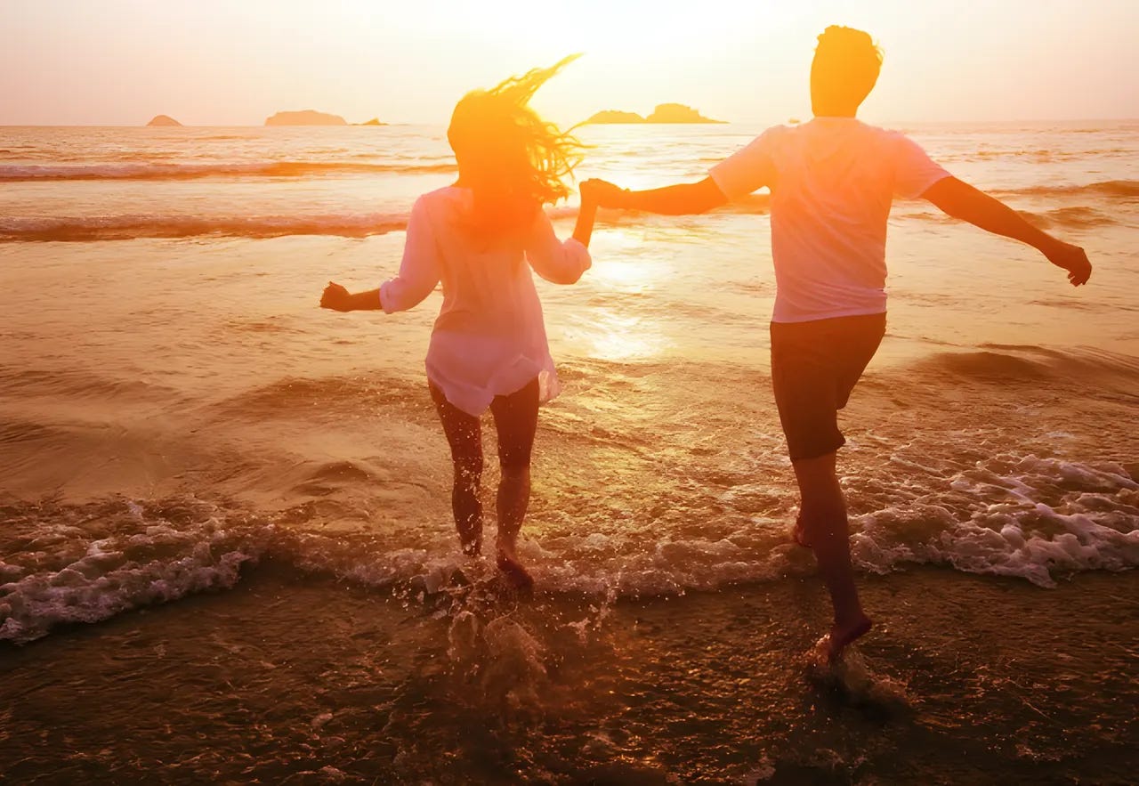 Couple splashing in the surf holding hands, silhouetted against the setting sun. Couple splashing in the surf holding hands, silhouetted against the setting sun.