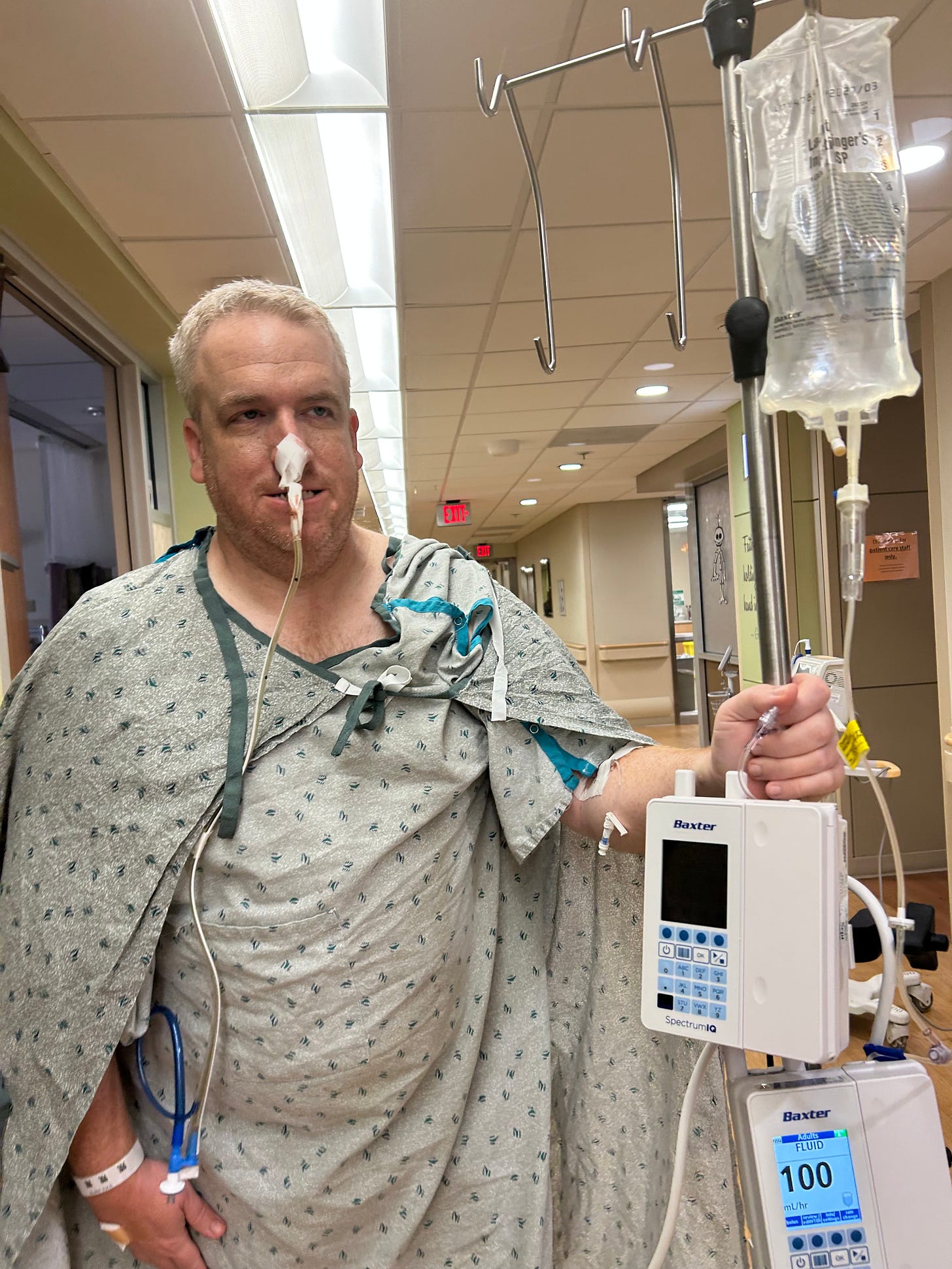 Adam walking through a hospital hallway during recovery from liver surgery while wearing a nasogastric tube and carrying medical equipment.