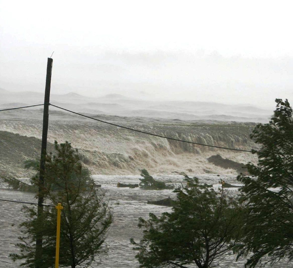 Hurricane Katrina storm surge about to hit Bay St. Louis, Mississippi, in 2005. The oncoming ocean rises like a cliff and extends to the horizon at the higher level. Photographer’s name unknown. It was someone on the staff of St. Stanislaus boarding school who stayed with any students who could not evacuate. The school is near the top of the bluff which is the highest point on the Gulf Coast west of Florida. The ground floor of the school was blown out by the storm surge. Staff and students were on the upper floor and survived.