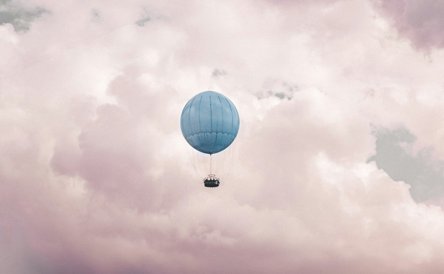 blue hot air balloon floating in the center of a pink clouds that look like cotton candy