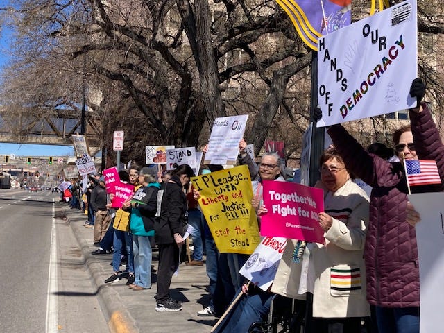 From top left - someone holds a sign saying "Billionaires are the only dangerous minority" in front of a truck with an upside down US flag; a large crowd carrying signs fills the lawn in front of a government building; a large group of people holding signs line a sidewalk; a large group of people with signs gather in a park, in the foreground is a sign that reads "Love is greater than fear" and an American flag.