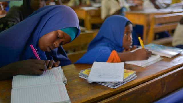 Students in a classroom, writing in books on desks