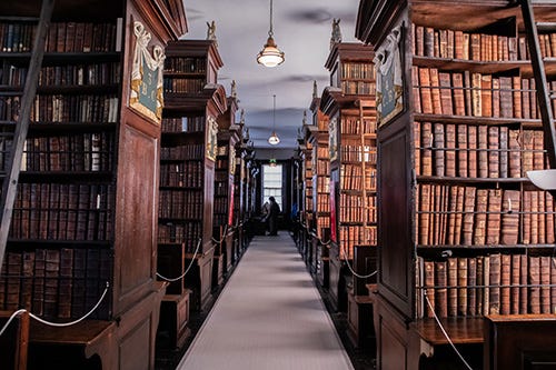 Looking along the aisle between rows of tall bookcases filled with leatherbound books.
