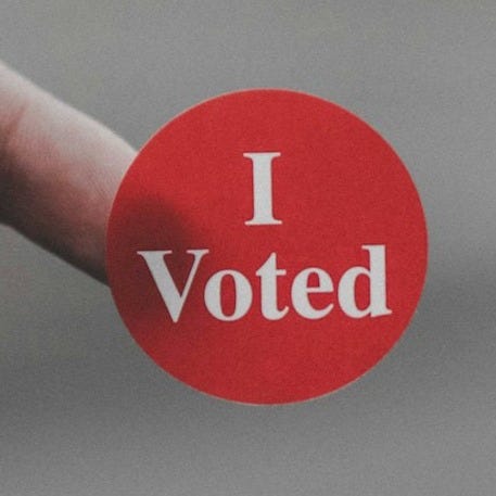 a hand holding a red button that says i vote