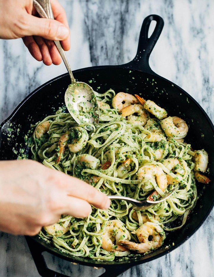 On the left, a wide bowl with smashed potatoes, cod, roasted lemons, microgreens, and a creamy sauce. On the right, a skillet with hands tossing noodles with shrimp and pesto.
