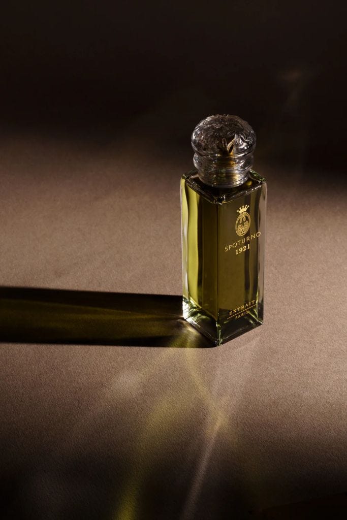 A beautifully designed glass perfume bottle with an ornate stopper, featuring a yellowish liquid inside, placed on a textured surface that casts a soft shadow.