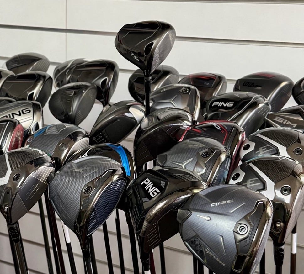 A row of second-hand golf drivers on a shop display, with several clubheads overlapping and one raised slightly above the others. A row of second-hand golf drivers on a shop display, with several clubheads overlapping and one raised slightly above the others.