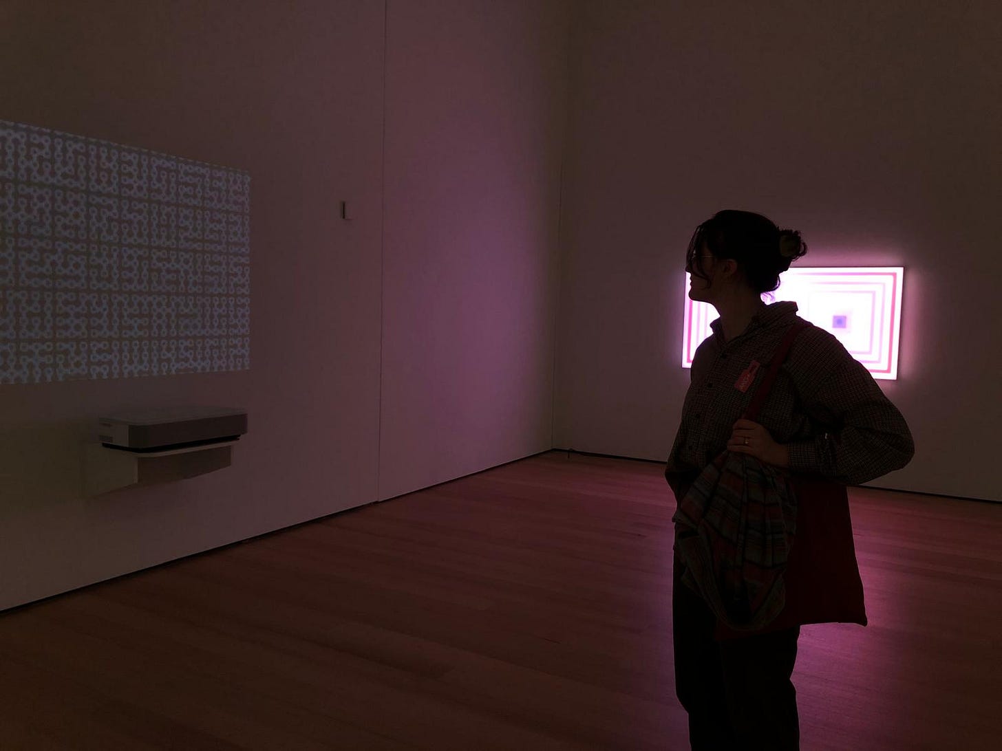 Jo is silhouetted by a pink/purple light while looking at a multimedia art installation