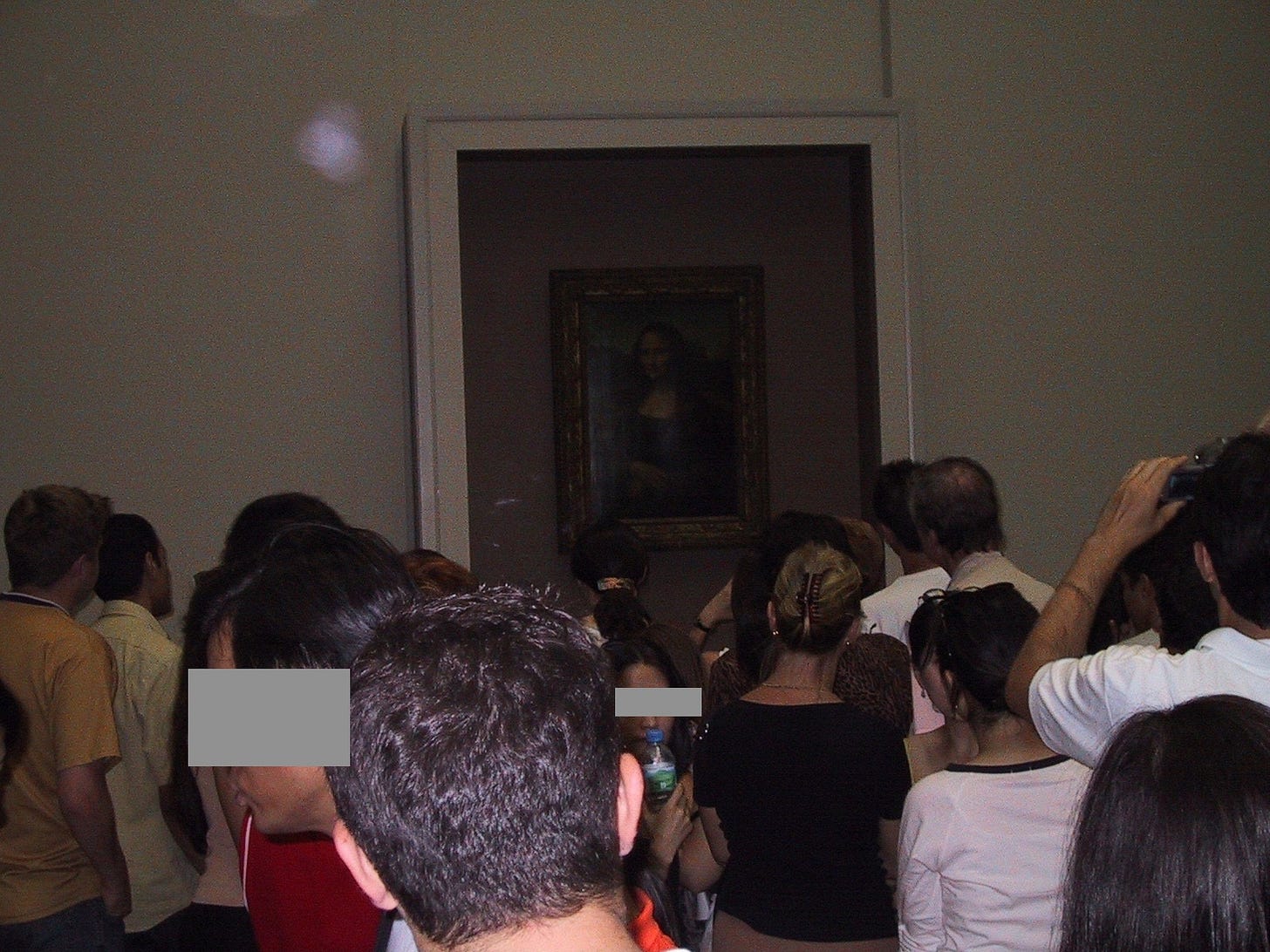 Photo taken by the author in 2002 on his first visit to the Louvre on a crowded summer’s day. The photo show a dim Mona Lisa behind protective glass. The majority of the photo succeeds in capturing the back of other people’s heads.