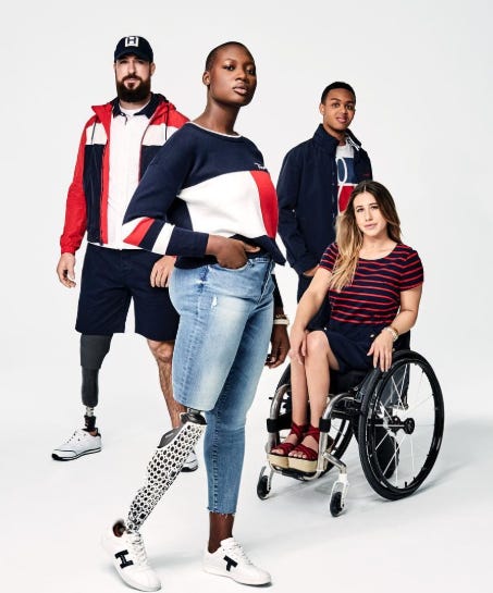 São 4 modelos em um fundo branco. Eles vestem roupas em tons branco, vermelho e preto. Os modelos são homens e mulheres, dois com amputação nas pernas, uma em cadeira de rodas e um homem sem deficiência física aparente. Fim da descrição.