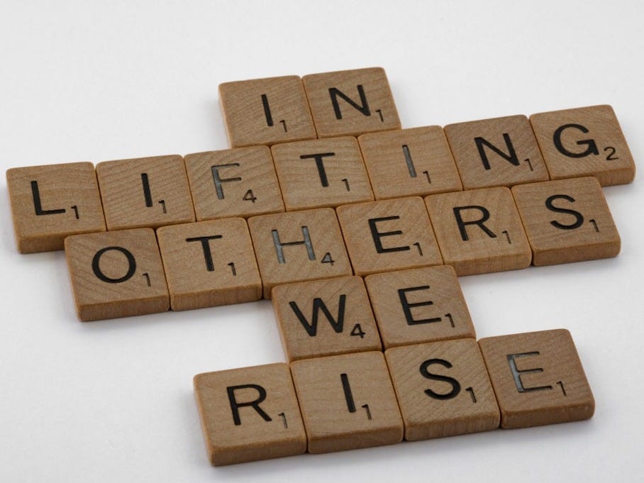 Brown wooden blocks on white table spelling out "In lifting others we rise" Brown wooden blocks on white table spelling out "In lifting others we rise"