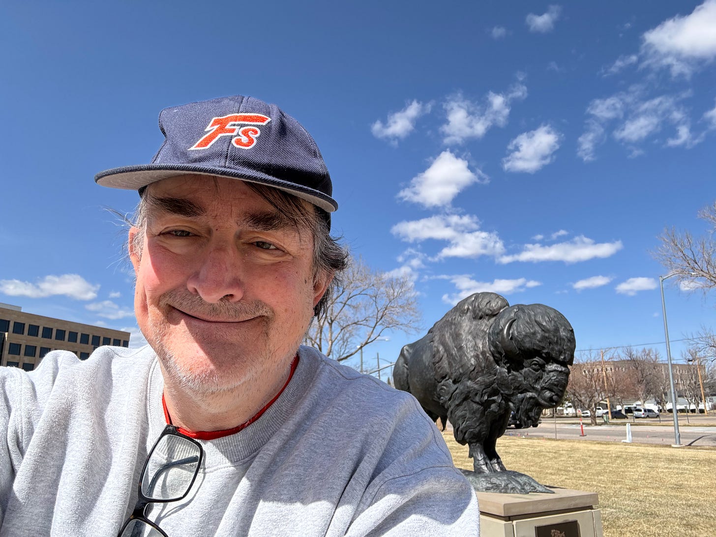 Author on lawn of Wyoming state capitol next to a statue of a bison