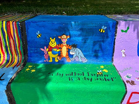 sections of the painted bench: Winnie the Pooh and friends, a rainbow, a book with a flower growing out of it.