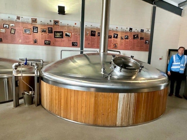 Inside the new Hall and Woodhouse brewery. Historical pictures in the background. In the foreground is the silver top of a brewing vat around 2 metres across, with a viewing porthole.