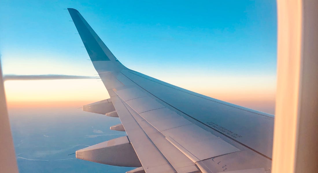 A plane window with the wing of a plane and a sunrise sky A plane window with the wing of a plane and a sunrise sky