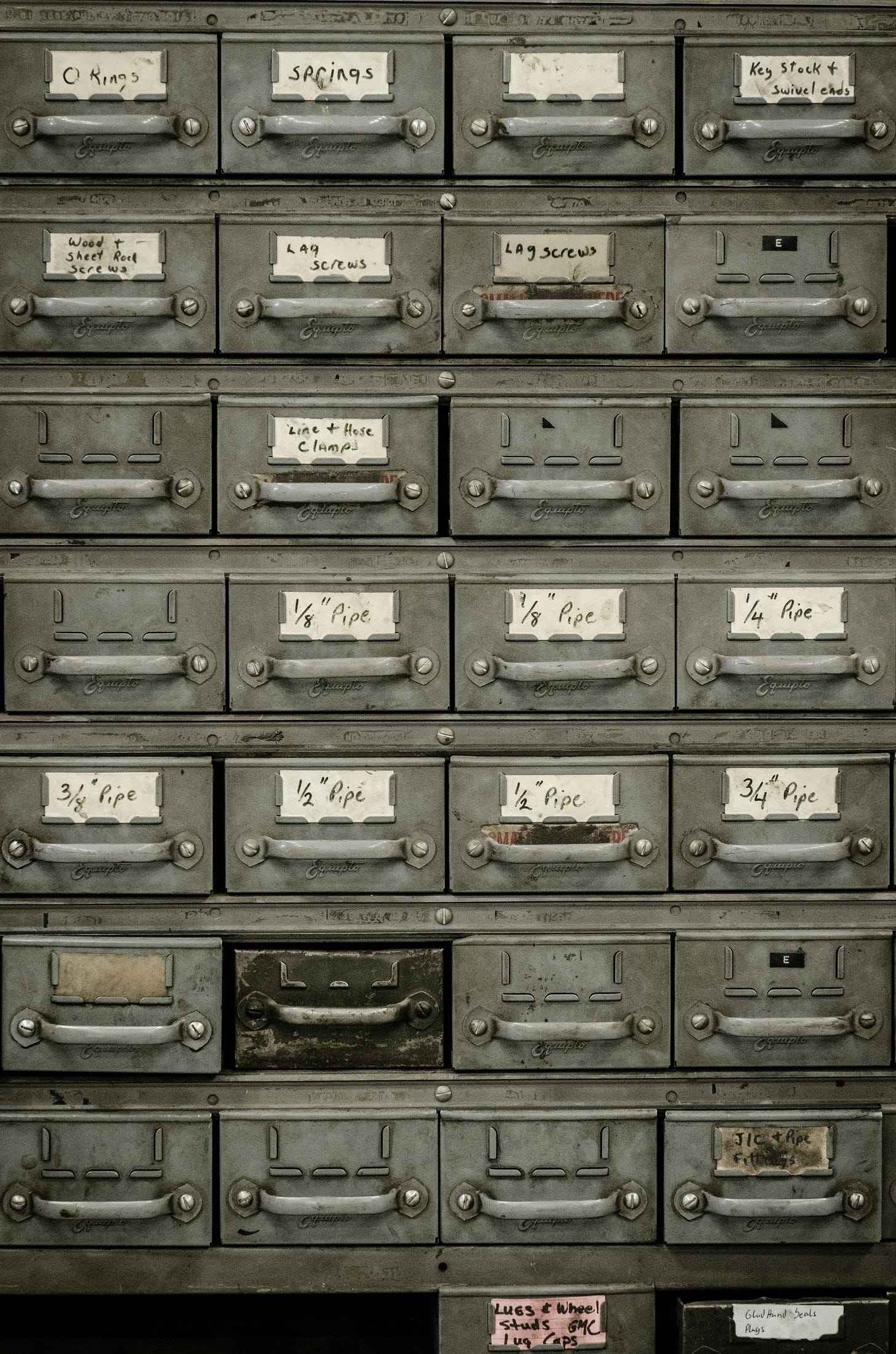 Photo of a set of 28 small metal drawers that look well-used, some with labels for hardware like springs, screws, and clamps