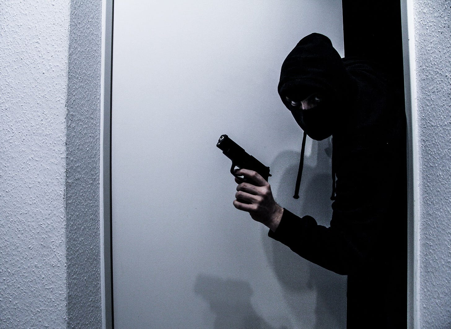 A burgler with a gun exits a doorway. A burgler with a gun exits a doorway.