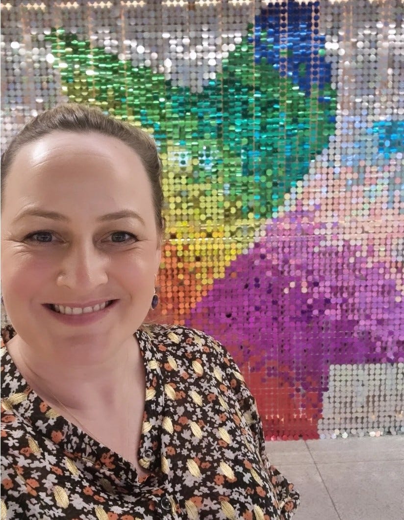 Briar smiling at the camera with a sparkly, rainbow NAB logo in the background. Briar smiling at the camera with a sparkly, rainbow NAB logo in the background.