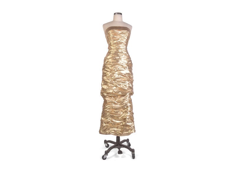 May include: A gold, strapless dress with a ruched design, displayed on a dress form. The dress is floor-length and has a textured appearance. The dress form is mounted on a wheeled base, suitable for a boutique or fashion display.