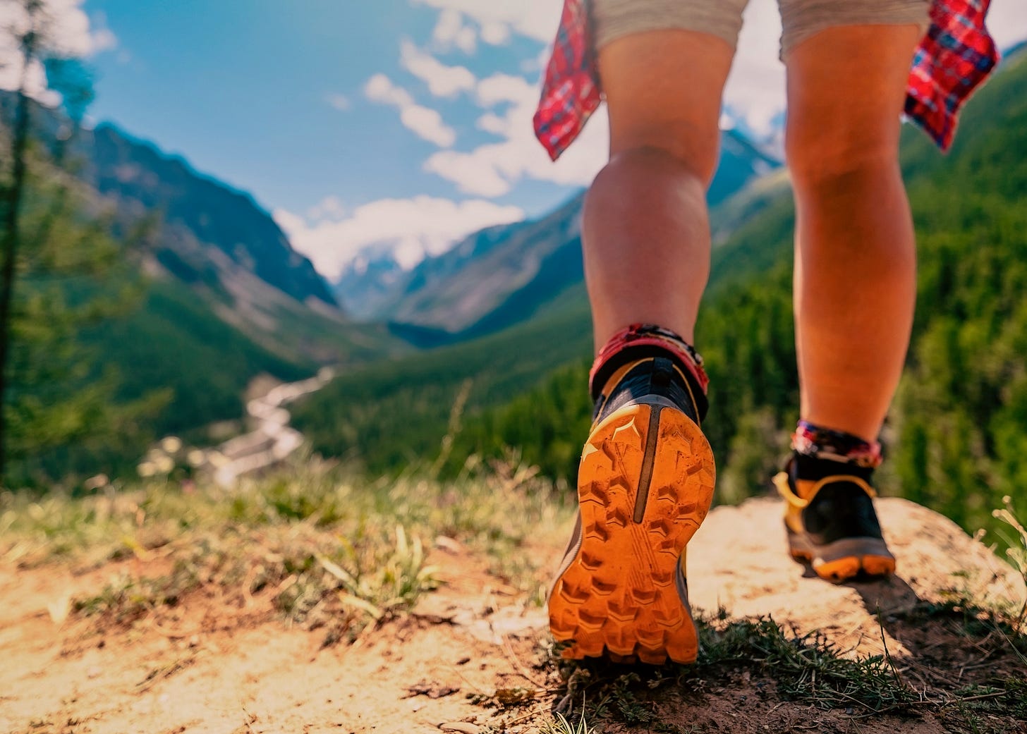 Photograph focuses on hikers shoes as she walks along a path through mountains. Photograph focuses on hikers shoes as she walks along a path through mountains.