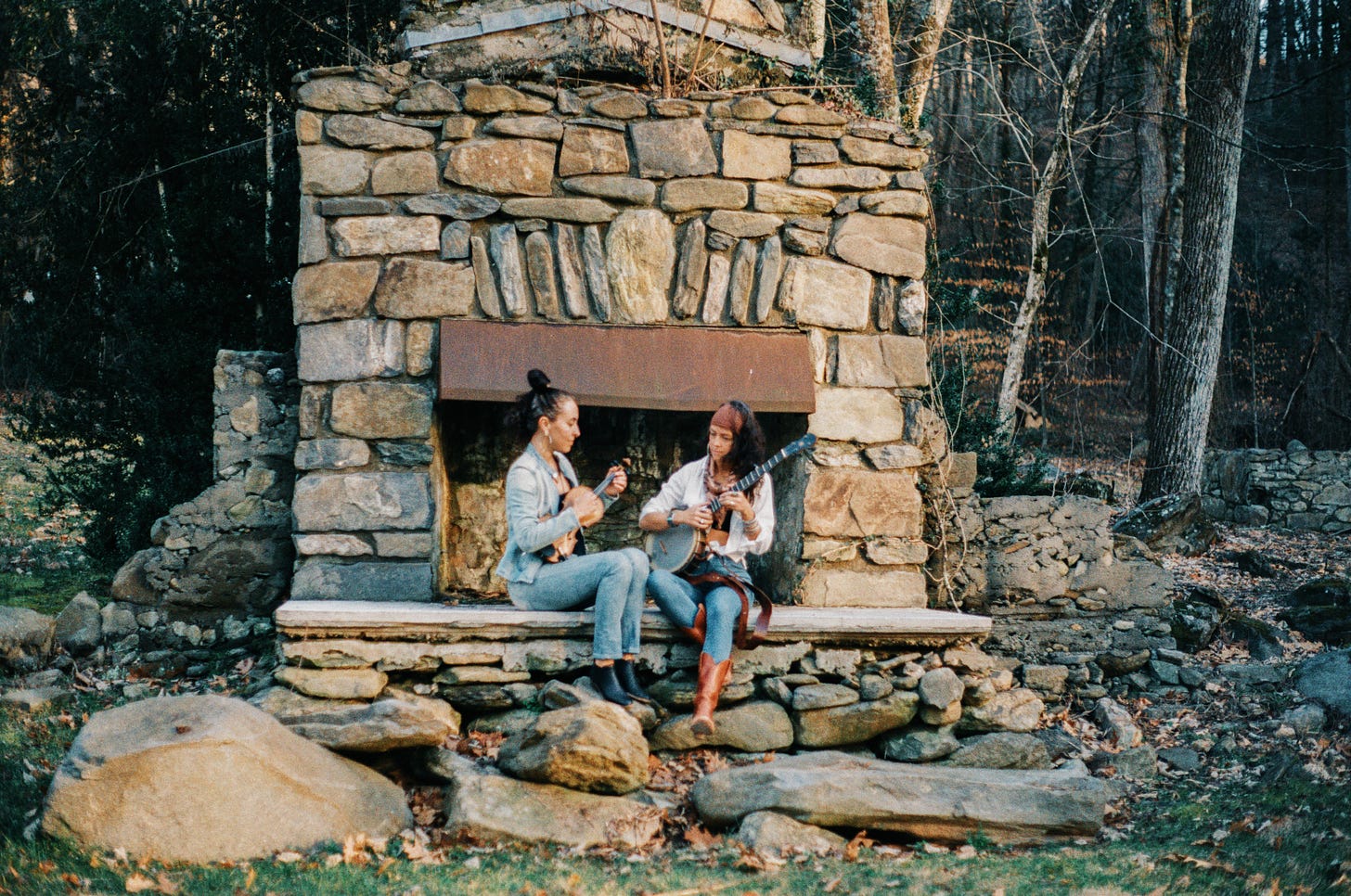 Two women sitting in front of a fireplace playing instruments