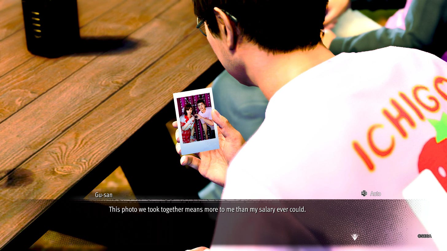 A character named Gu-san holding a photo of him next to an idol he is a fan of. He is making a half heart with his hand, while she makes a thumbs up with her hand. Gu-San says: "This photo we took together means more to me than my salary every could."