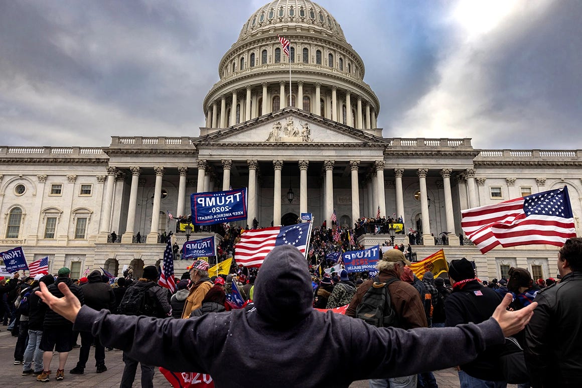 A man throws his head back and arms out in from the U.S. capitol as rioters charge the stairs.