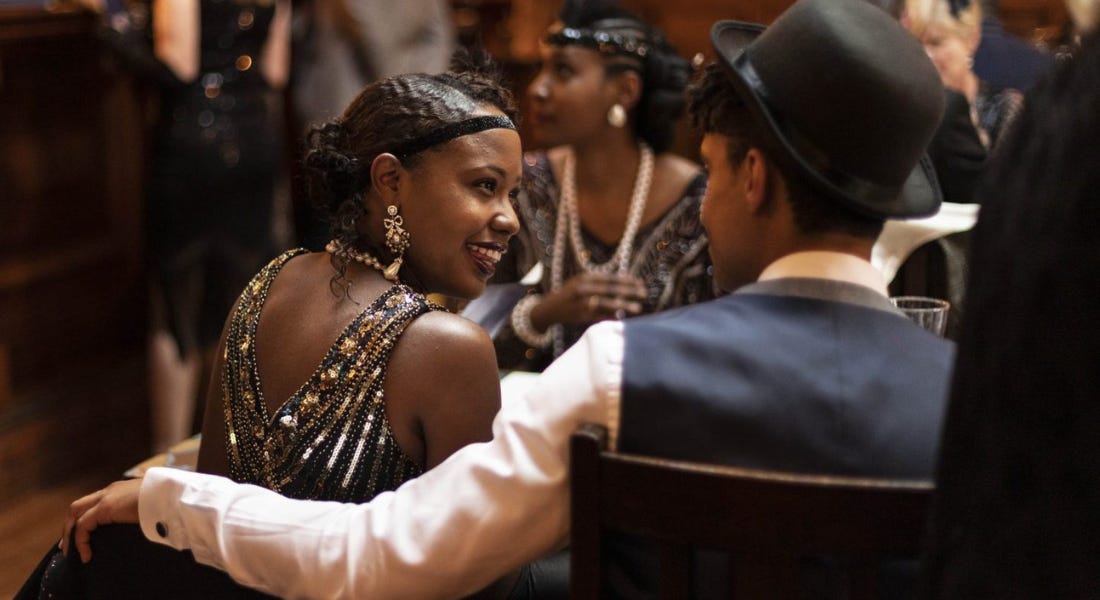 A man and a woman dressed in 1920s style outfits sitting down and facing each other