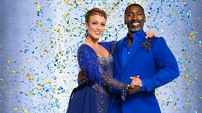 Lauren wears a dark blue glittering dress with blue fringe trim on the shoulders. Jimmy wears a deep blue suit.