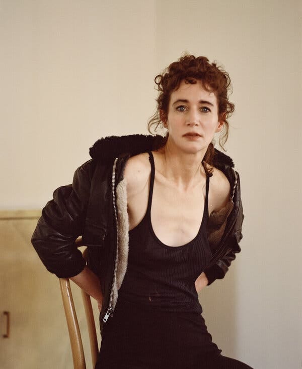 Sitting on a chair, Ms. July wears a black spaghetti-strap tank top underneath a leather jacket with fleece trim. Sitting on a chair, Ms. July wears a black spaghetti-strap tank top underneath a leather jacket with fleece trim.