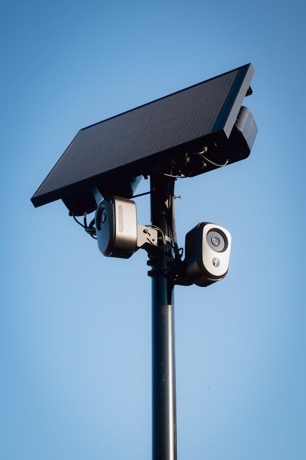 A close-up of a Flock camera on a pole, with a solar panel above it.