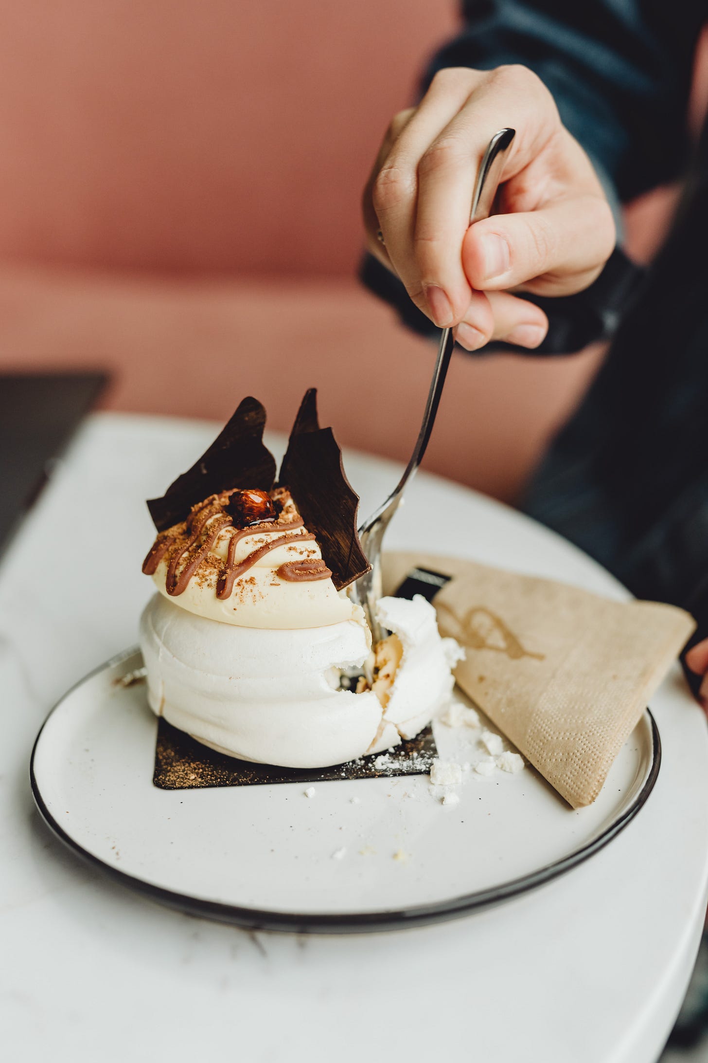 person's arm in the photo holding a fork digging into a dessert made with meringue on a white plate