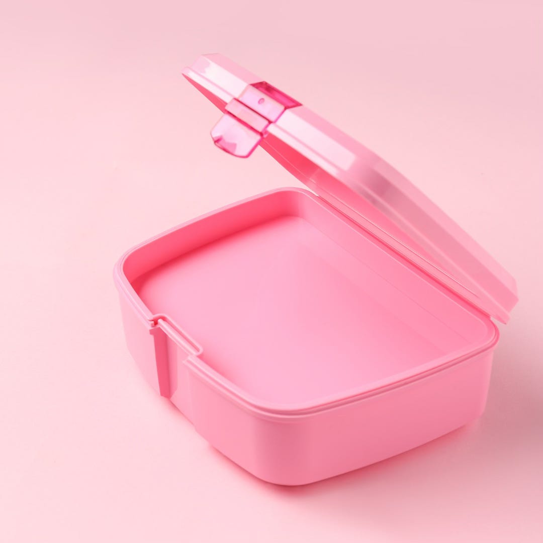 A photo of an empty pink lunch box against a pink background.