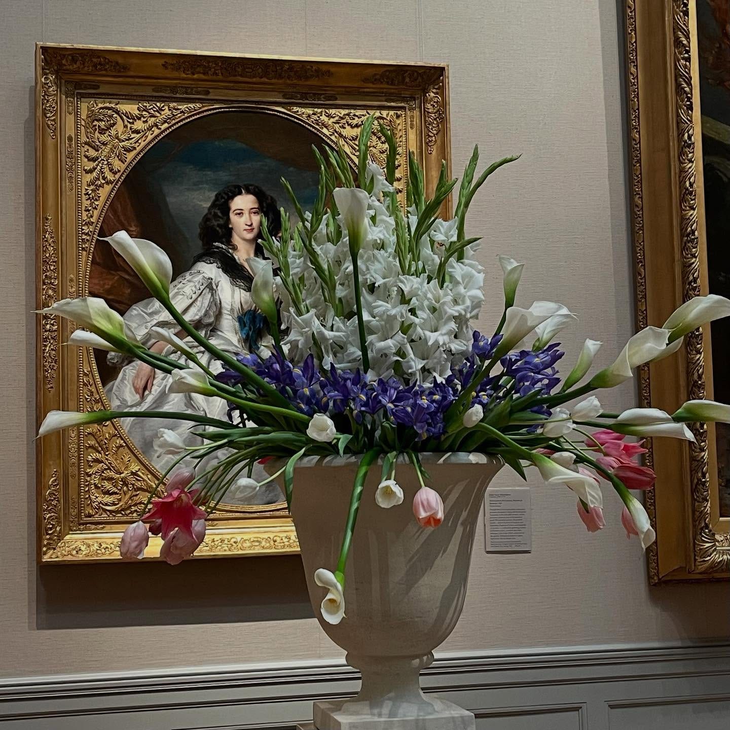 May be an image of 1 person, flower arrangement, urn, lily of the Nile and text