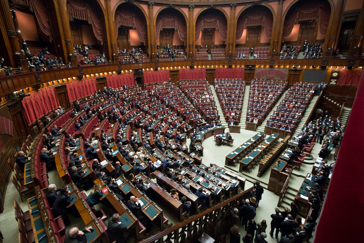 Italian Parliament Chamber of Deputies in session with legislators seated in semicircular red upholstered benches in ornate parliamentary hall with classical architecture and balcony galleries Italian Parliament Chamber of Deputies in session with legislators seated in semicircular red upholstered benches in ornate parliamentary hall with classical architecture and balcony galleries