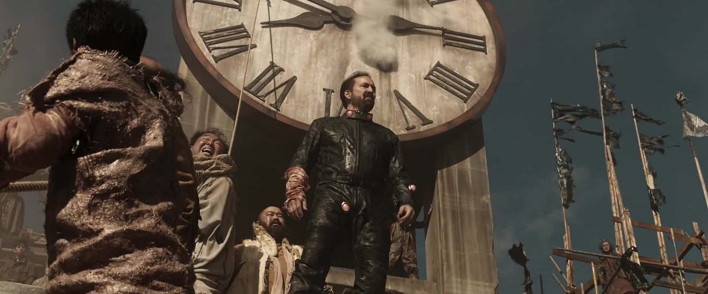 Nicholas cage in leather standing in front of a giant clock; Japanese men are hauling on a rope next to him