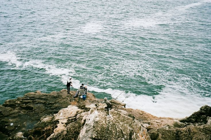This may contain: two people standing on rocks near the ocean