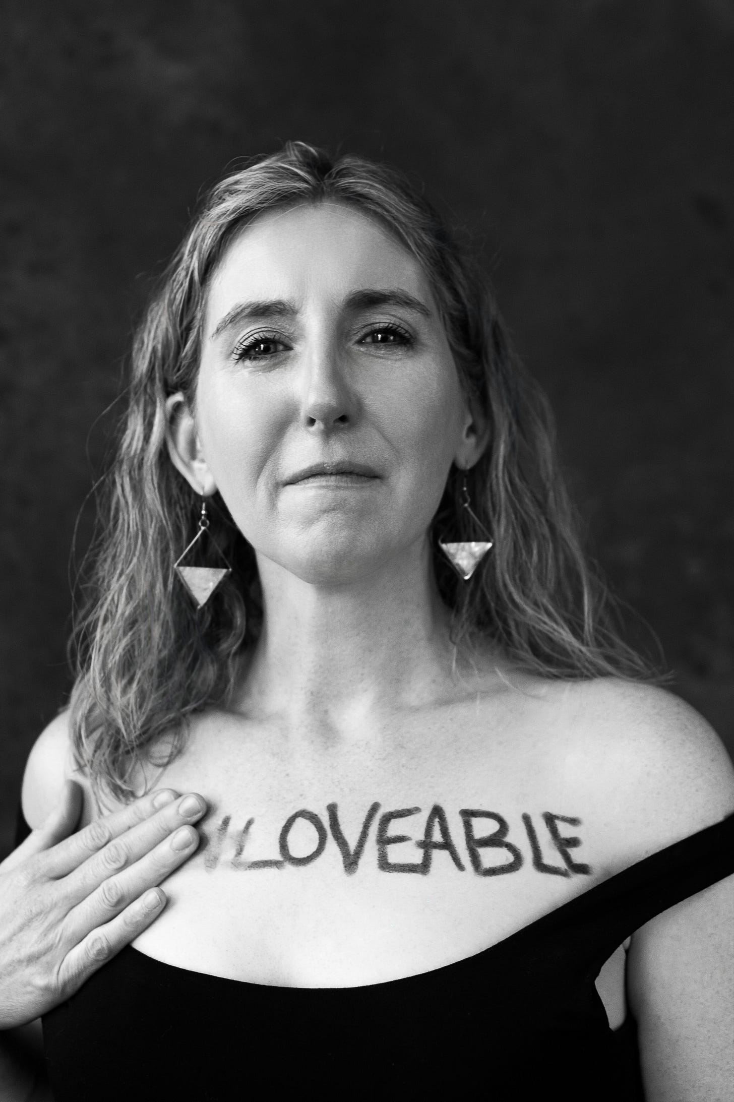 Woman crying while wiping off the words "unloveable" from her chest