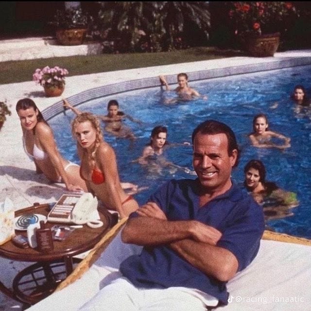This may contain: a man sitting in front of a swimming pool surrounded by other women and men around it