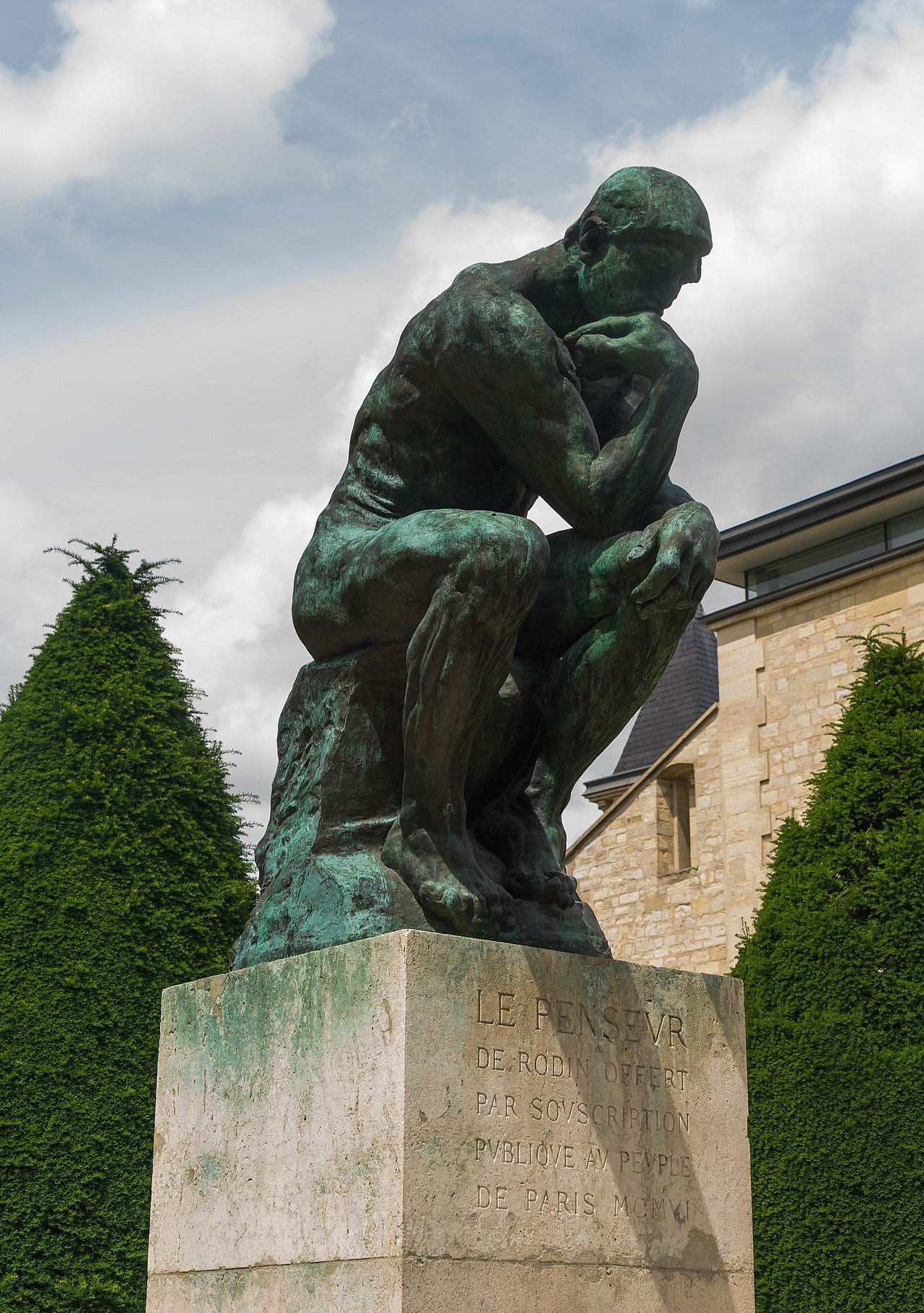 Rodin's The Thinker, a bronze man seated on a rock with his chin on his hand, in the garden of the Musée Rodin