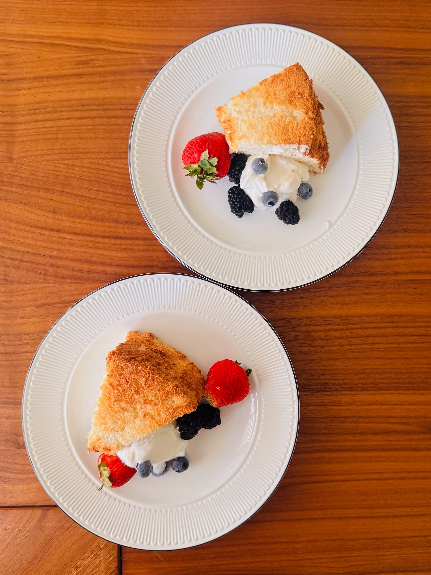 Angel food cake topped with fresh strawberries, blueberries, blackberries, and whipped cream on a white cake plate Angel food cake topped with fresh strawberries, blueberries, blackberries, and whipped cream on a white cake plate