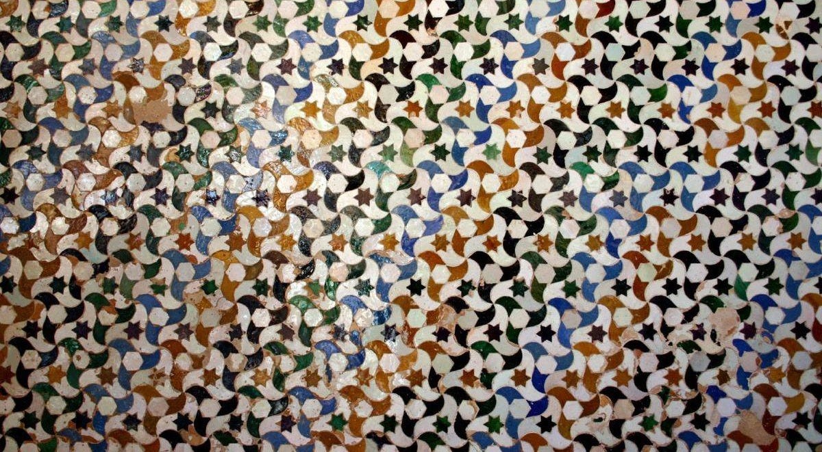 Glazed tile mosaic in the Alhambra, Granada: interlocking curved tiles in green, blue, ochre and black around small dark stars Glazed tile mosaic in the Alhambra, Granada: interlocking curved tiles in green, blue, ochre and black around small dark stars