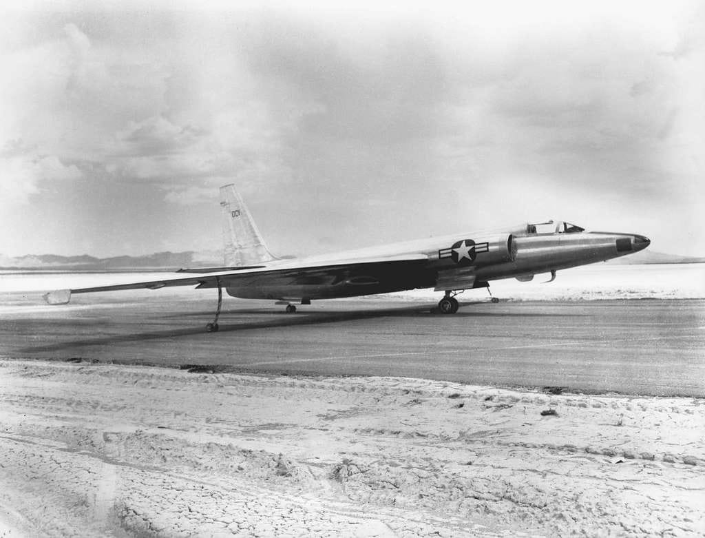 Archival black-and-white photo of a long-winged U.S. high-altitude U-2 reconnaissance jet preparing for a first flight (August 4, 1955) parked on a dry airfield, with desert mountains in the background and thin landing gear extended.