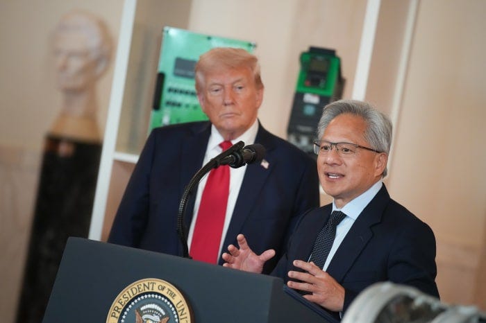 Nvidia CEO Jensen Huang speaks at a lectern as President Trump listens behind him.