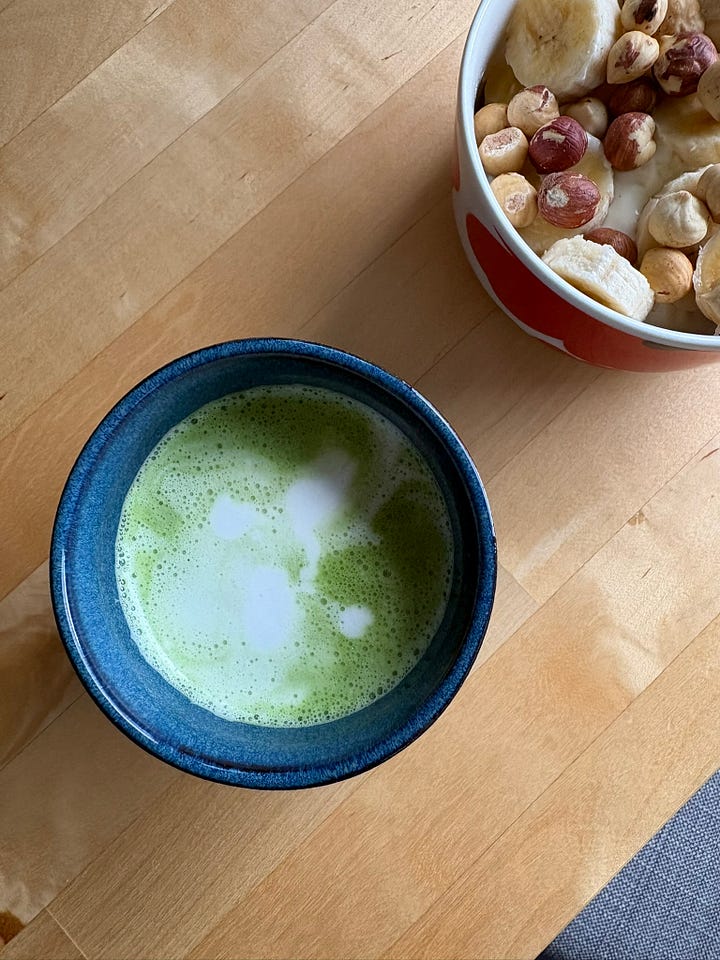 A slice of toast with butter, honey and tea. A matcha latte on a dining table with breakfast in the background