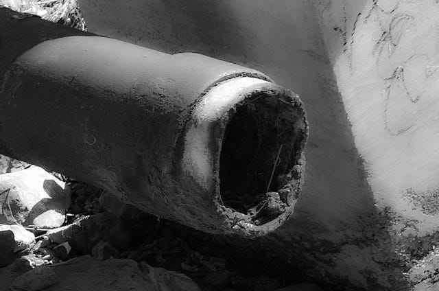 Rusty metal culvert jutting through the concrete seawall