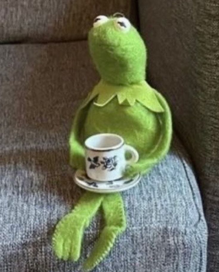 This may contain: kermie the frog holding a coffee cup and saucer on top of a couch This may contain: kermie the frog holding a coffee cup and saucer on top of a couch