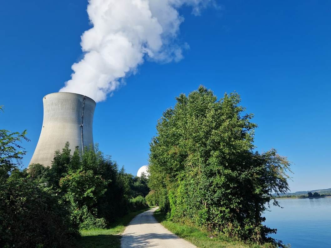 Cooling tower of the nuclear power plant. rhine on the right, hiking route between the two. bushes and trees on either side of the path.